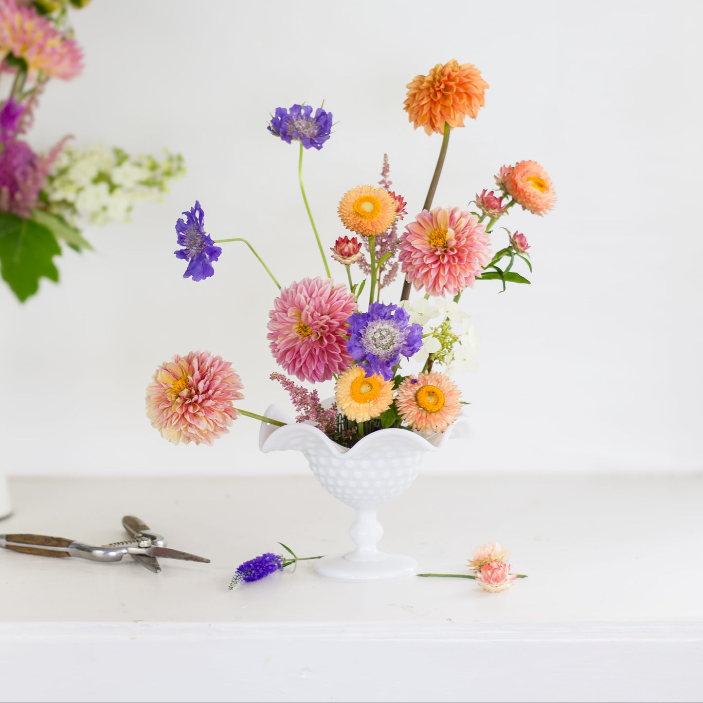 Brightly colored flowers in a hairpin holder flower frog and footed white vase